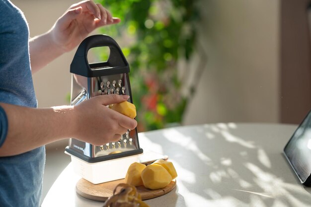 Uma menina rala batatas recém-descascadas para fazer panquecas de batata