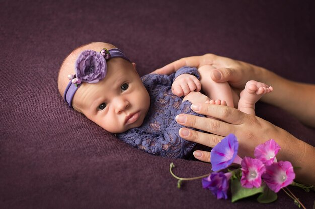 Uma menina recém-nascida é segurada pelas mãos de sua mãe em um fundo roxo com flores