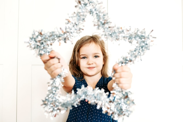 Uma menina segura uma estrela nas mãos para decorar a casa para o ano novo e o natal, a criança se prepara para o feriado, ajudando os pais, esperando os presentes