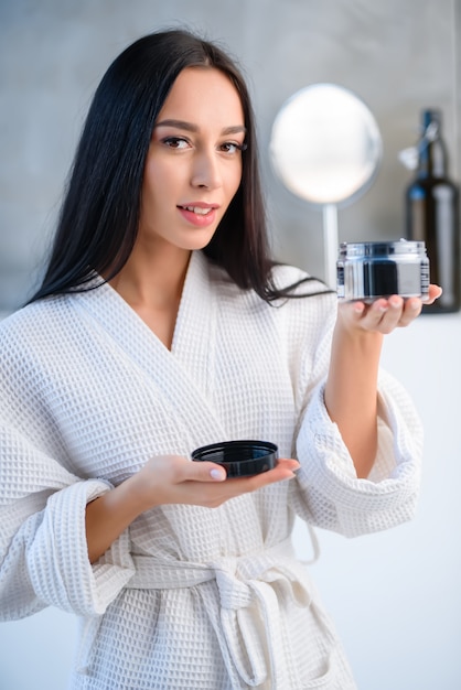 Uma menina segura uma lata redonda com produtos para os cabelos no banheiro