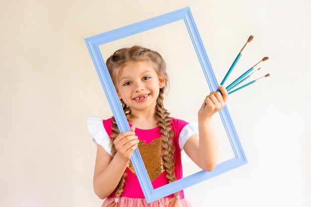 Uma menina segura uma moldura azul e um conjunto de pincéis.