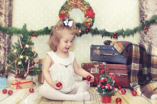 Uma menina sentada em frente a uma árvore de Natal brincando com brinquedos