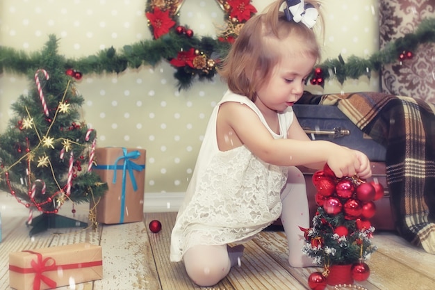 Uma menina sentada em frente a uma árvore de Natal brincando com brinquedos