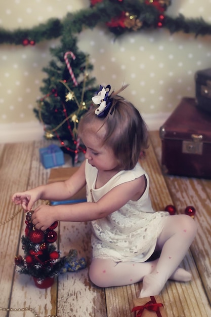 Uma menina sentada em frente a uma árvore de natal brincando com brinquedos