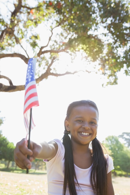 Uma menina sentada na grama, acenando a bandeira americana em um dia ensolarado