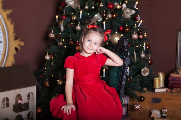 Uma menina sentada na sala perto da árvore de Natal