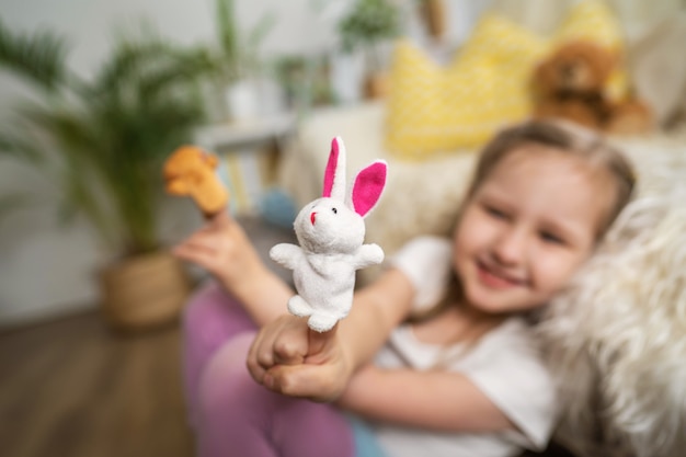 Uma menina sentada no chão, apoiando-se na diversão de sofand brincando com brinquedos de dedo