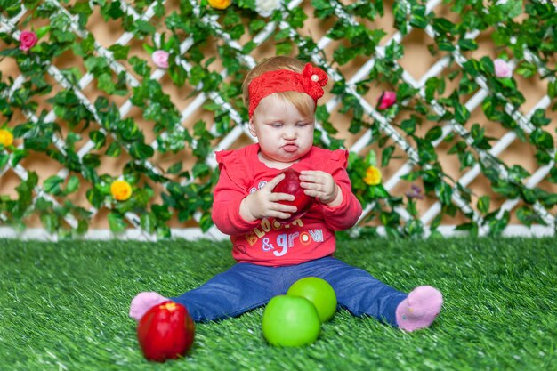 Uma menina sentada no parque na grama em dia de verão ensolarado e brincando com maçãs