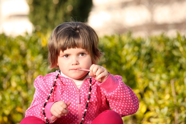 uma menina sentada no parque tentando usar um brilho labial