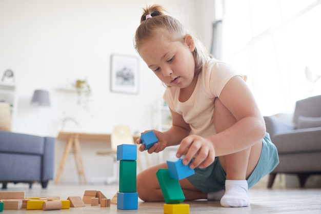 Uma menina sentada no sofá brincando com blocos coloridos ela construindo uma pirâmide em casa