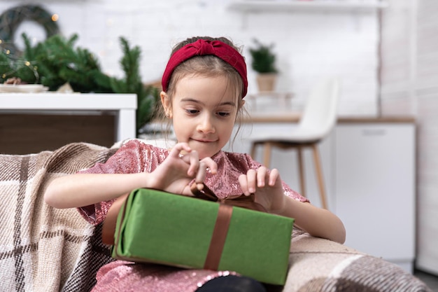 Uma menina sentada no sofá com uma caixa de presente fica feliz com o presente