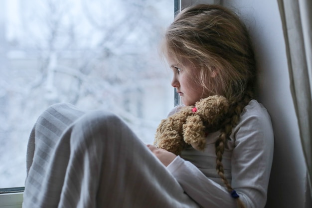 Uma menina solitária senta e olha tristemente pela janela