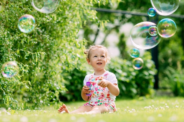 Uma menina sopra bolhas de sabão no parque sentada na grama o conceito de uma infância feliz