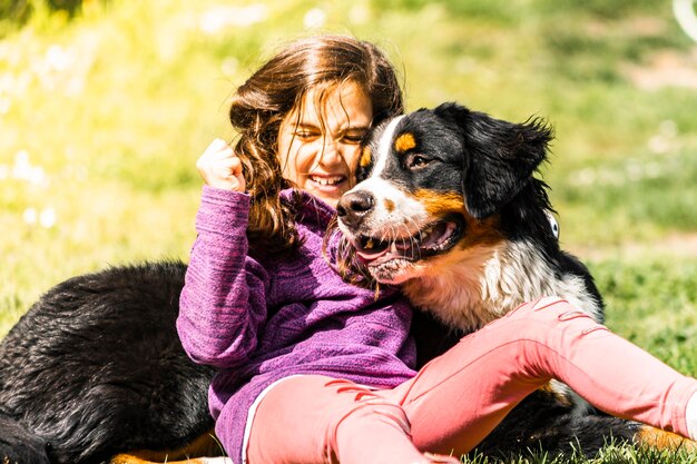 Foto uma menina sorridente a brincar com um cão na grama.