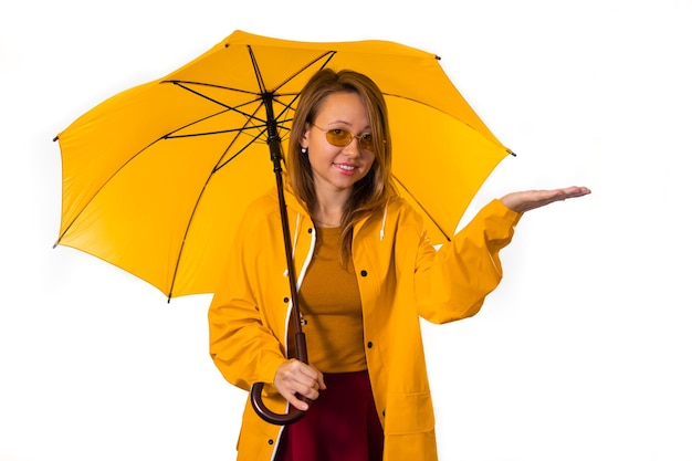 Uma menina sorridente com uma capa de chuva amarela está sob um guarda-chuva e estende a mão na chuva