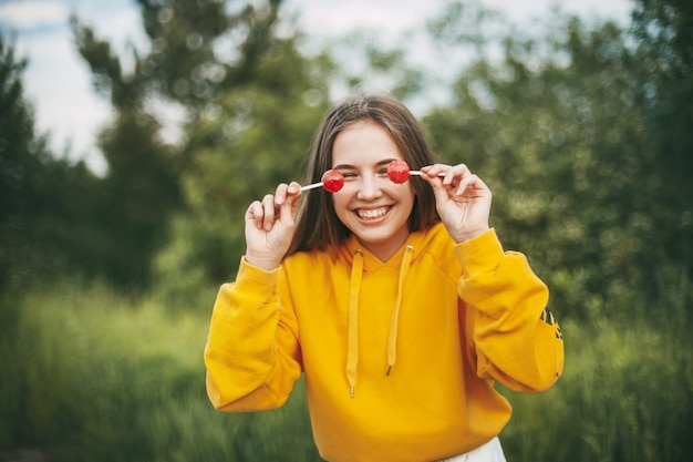 Uma menina sorridente em um suéter amarelo brilhante segura um pirulito vermelho brilhante