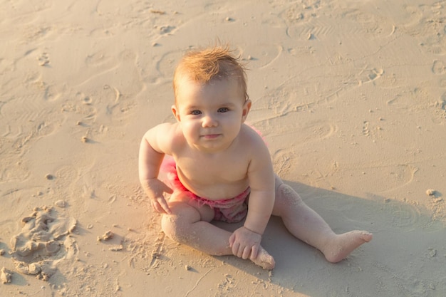 Uma menina sorridente está sentada em uma praia de areia perto do mar na luz do sol ao pôr do sol