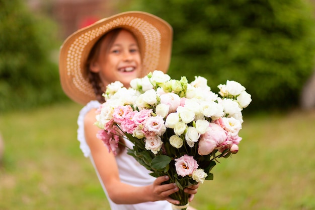 Uma menina sorridente tem um lindo buquê de peônias rosa e brancas nas mãos dela.