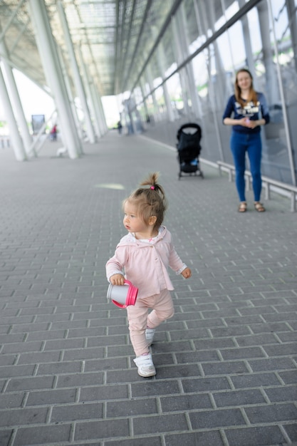 Uma menina tenta andar sozinha um edifício moderno. Na mão de uma garota segurando uma xícara de derramamento.