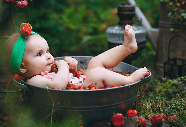 Uma menina toma banho em uma bacia com morangos no jardim.