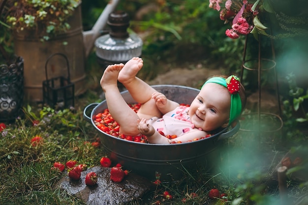 Uma menina toma banho em uma bacia com morangos no jardim.