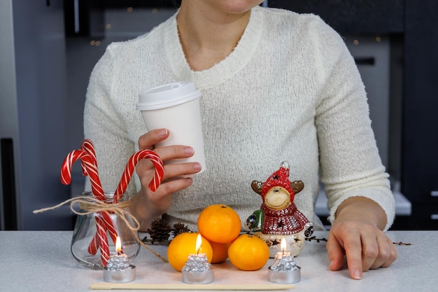 Uma menina Três Mandarins pauzinhos uma estatueta de Natal e doces em uma mesa branca contra um fundo escuro da cozinha