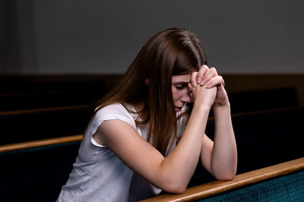 Uma menina triste christian na camisa branca está sentado e orando com coração humilde na igreja