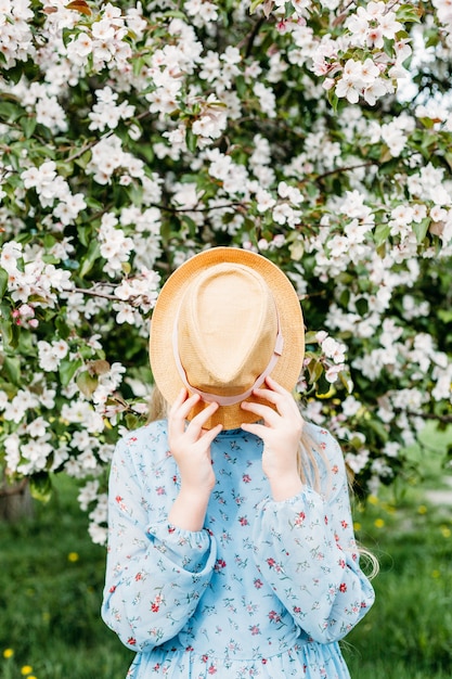 Foto uma menina, uma adolescente de chapéu anda na primavera na cidade, árvores floridas, uma macieira, o rosto não é visível