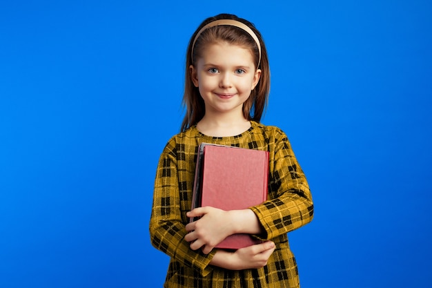 Uma menininha em um vestido casual segurando livros contra um fundo azul