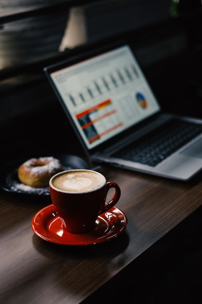 Uma mesa com um laptop mostrando gráficos, uma xícara de café e um donut