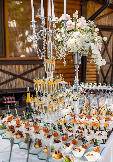 Uma mesa com uma variedade de aperitivos e bebidas, incluindo uma pilha alta de copos de champanhe