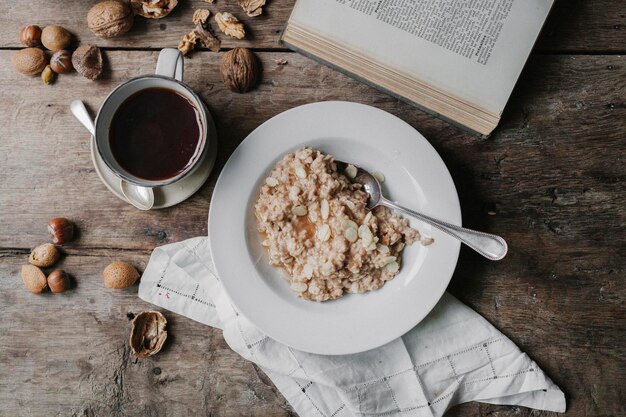 Uma mesa com uma xícara de café com nozes muesli e um livro aberto