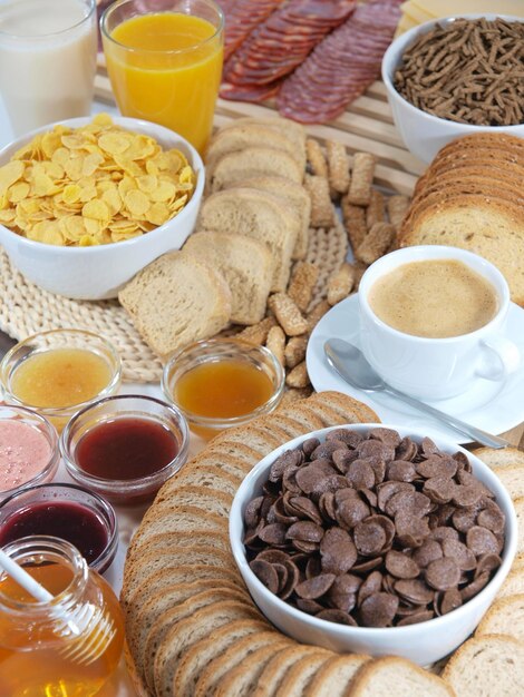 Uma mesa de café da manhã com muita comida, incluindo uma tigela de gotas de chocolate, uma xícara de café e um copo de suco de laranja.