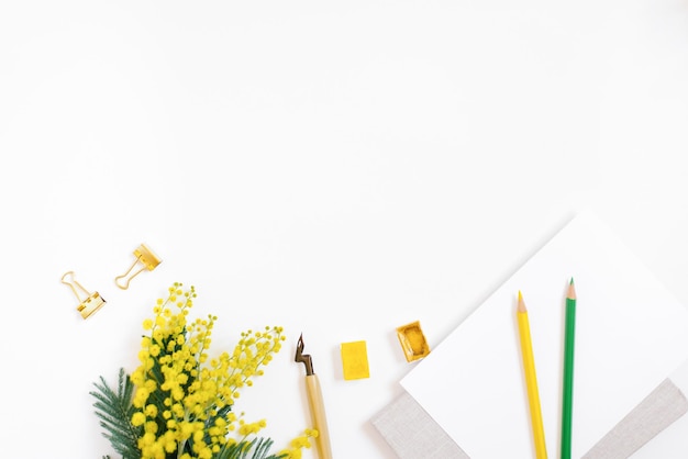 Uma mesa de escritório doméstica moderna de um blogueiro ou estudante com um caderno de papel, uma caneta para lápis coloridos de caligrafia e flores mimosas em um fundo branco com um espaço de cópia com