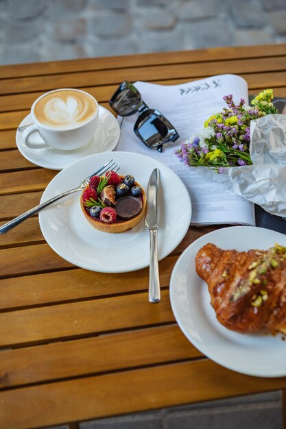 Uma mesa de madeira com óculos de sol de utensílios de café de sobremesa e uma revista