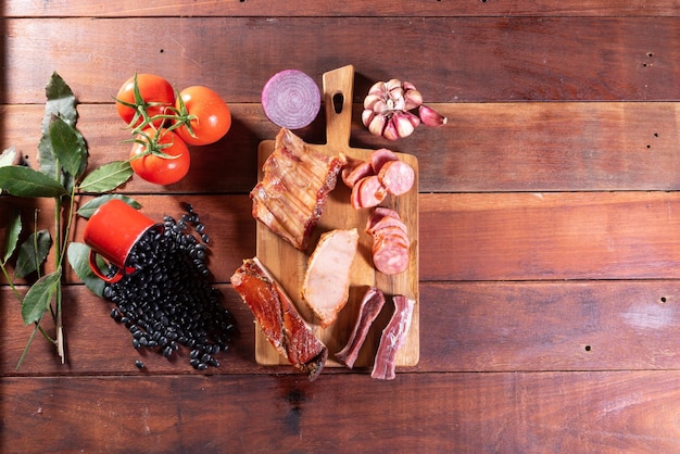 Uma mesa de madeira com uma tábua de corte com carne e legumes.