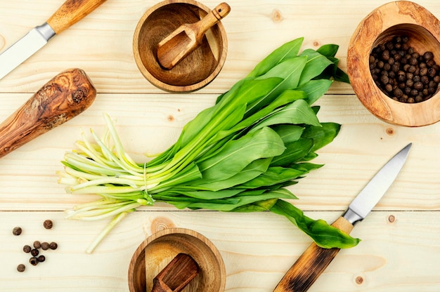 Uma mesa de madeira com vários utensílios de cozinha, incluindo um monte de folhas verdes.