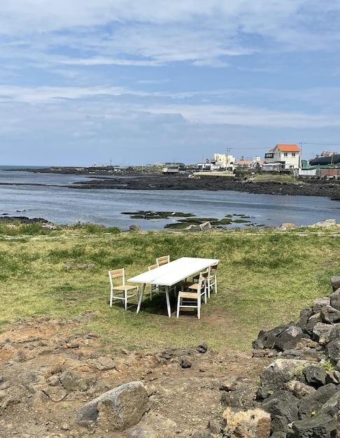 Uma mesa e cadeiras estão dispostas em uma área gramada com vista para o mar.