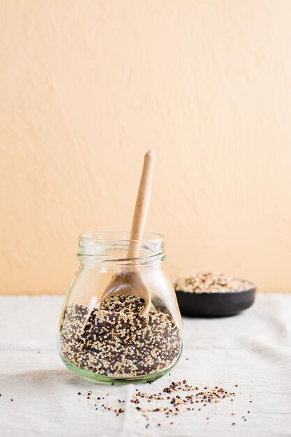 Uma mistura de quinoa vermelha e preta branca crua e uma colher de pau em uma jarra em um pano Comida saudável sem glúten Vista vertical