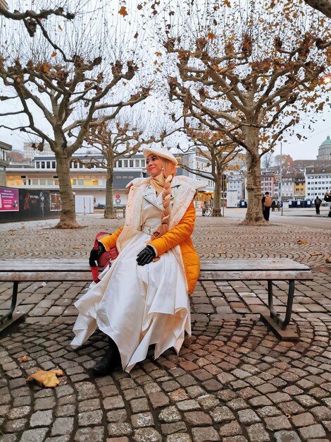 Foto uma modelo asiática sentada no banco na calçada com uma roupa branca elegante e uma jaqueta amarela