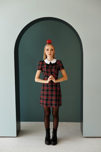 Uma modelo em um vestido xadrez com uma maçã na cabeça e maquiagem de outono em um estúdio fotográfico. Imagem de halloween