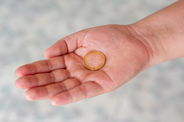 Uma moeda real na palma da mão de uma pessoa Mão segurando uma moeda de 1 dólar Real é o sistema monetário do governo brasileiro