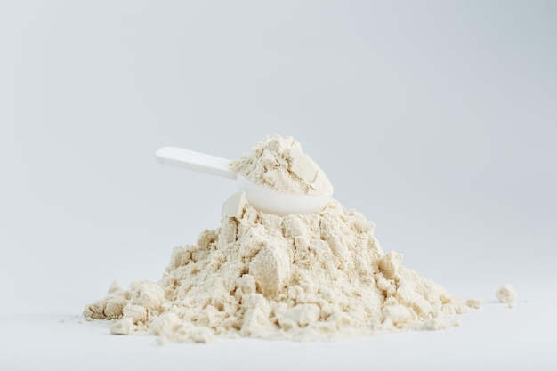 Uma montanha de proteína de soja isolada em pó com uma colher de medida em um fundo branco. Nutrição esportiva vegetariana para coquetéis