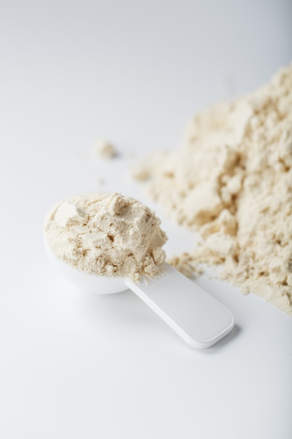 Uma montanha de proteína de soja isolada em pó com uma colher de medida em um fundo branco.