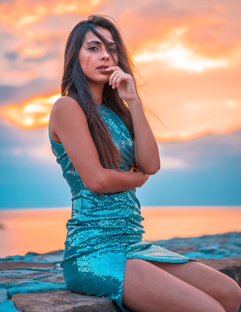 Uma morena bonita em um belo pôr do sol em um vestido azul de lantejoulas bodycon