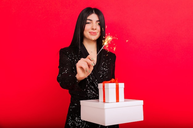 Uma morena de vestido preto com caixas de presentes e estrelinhas em um conceito de Natal de fundo vermelho