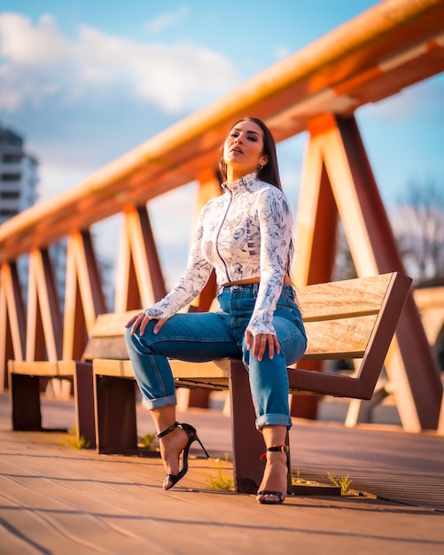 Uma morena latina na cidade ao pôr do sol em uma ponte laranja Posando do sentado