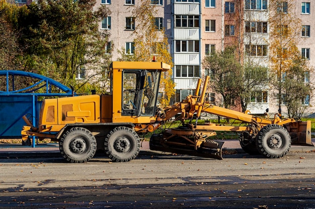 Uma motoniveladora realizando obras rodoviárias no centro de uma cidade moderna. A estrada funciona no outono.