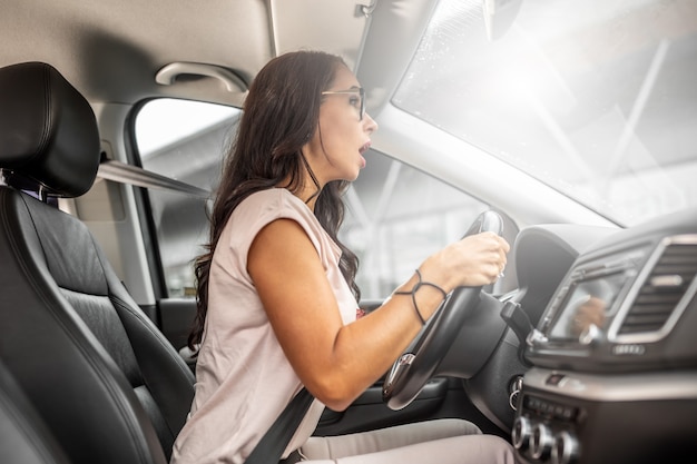 Foto uma motorista inexperiente está sentada atrás do volante bem perto, com a boca aberta e uma expressão assustada.