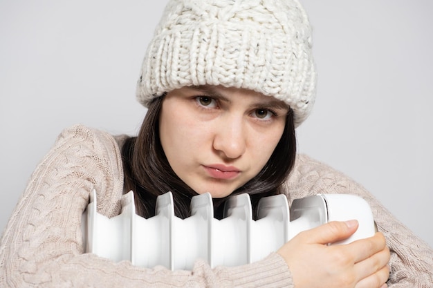 Uma mulher abraça um aquecedor elétrico a óleo e parece triste